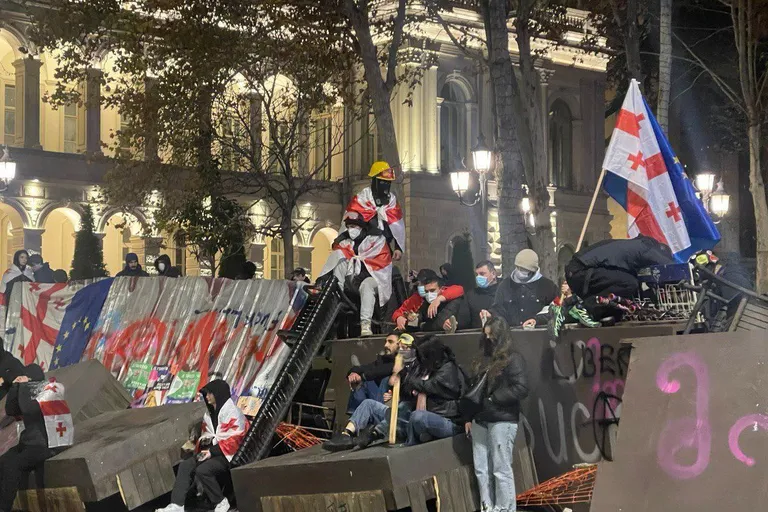 Баррикада в Тбилиси в полутьме. Многие люди на баррикаде в масках, у них флаги Грузии, ЕС и Украины.
