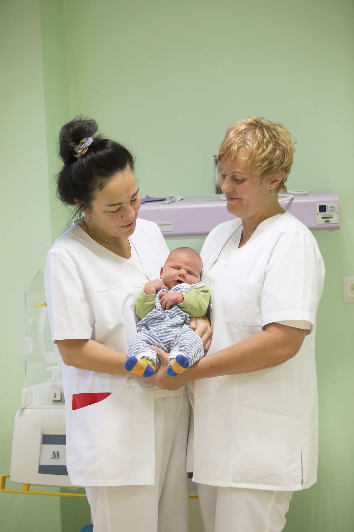 Lende Liivaste (vasakul) ja Janika Peep vaatavad heldimusega beebit, kes hiljaaegu ilmale tulnud ja nüüd emaga haiglas kosumas on.