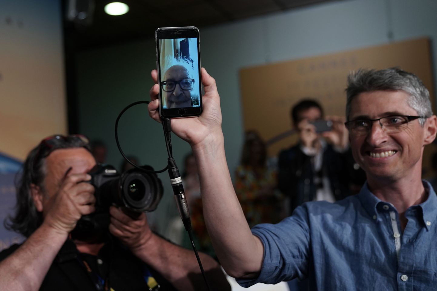 Vanameister Jean-Luc Godard ilmus pressikonverentsile telesilla abil oma kodust. Pildil Godard näha mobiiltelefonist, mida hoiab Šveitsi filmitegija Fabrice Aragno.