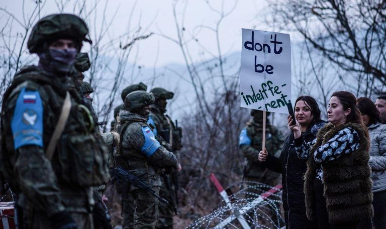 Женщины с плакатом «Не будьте безучастны» стоят перед российскими миротворцами