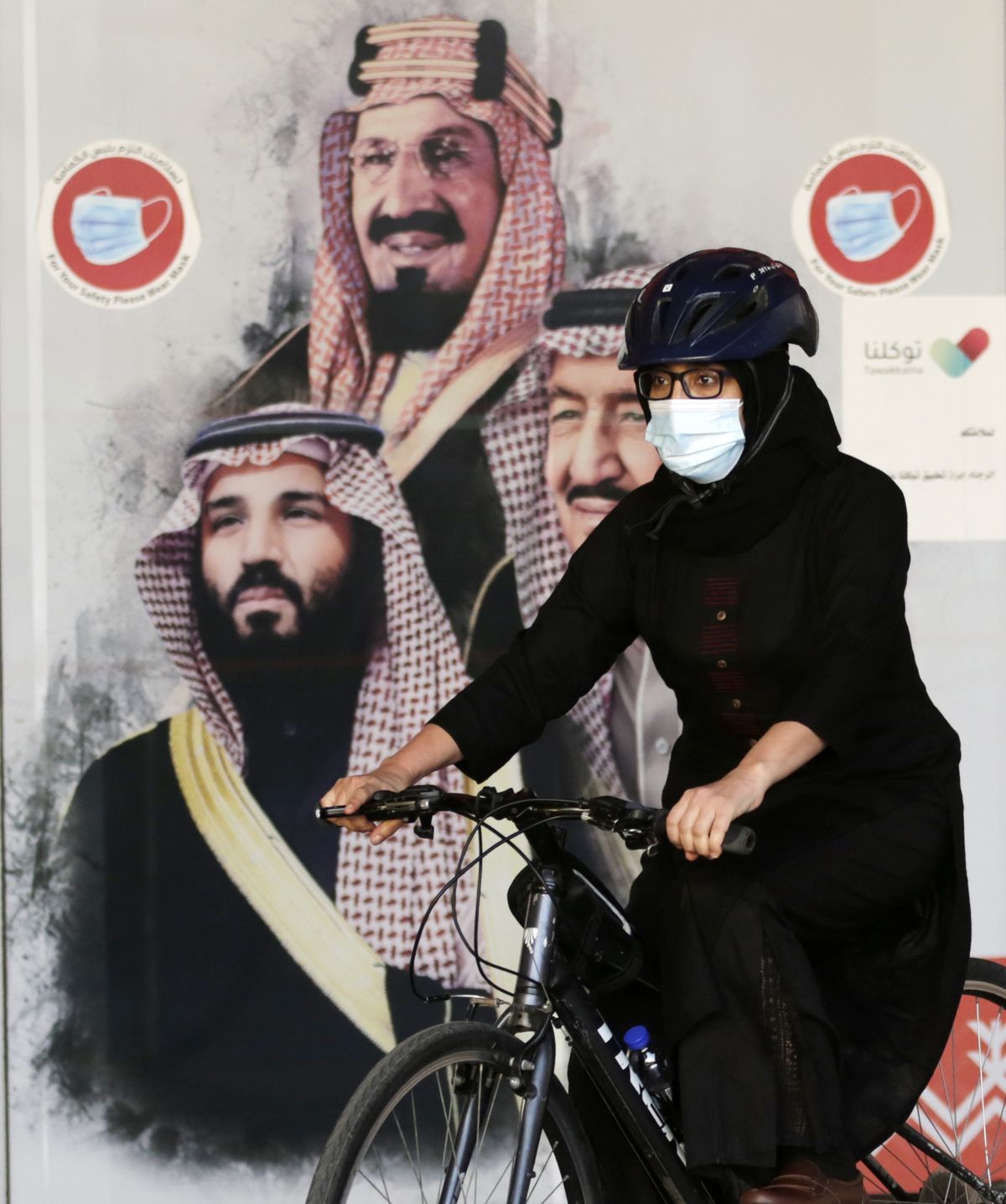 2021. gada 6. marts, Saūda Arābija, Džida. Sieviešu riteņbraucēju komandas dalībniece Amala brauc ar velosipēdu gar reklāmkarogu, kurā redzams Saūda Arābijas karalis Salmans, pa labi kroņprincis Mohammeds bin Salmans un pa kreisi - Saūda Arābijas dibinātājs, bijušais karalis Abduls Azizs Al Sauds. Sieviešu riteņbraucēju komanda tika izveidota 2019. gadā ar mērķi popularizēt sieviešu sportu. Pirms Starptautiskās sieviešu dienas riteņbraucējas organizē publisku velobraucienu, lai pievērstu sabiedrības uzmanību. 