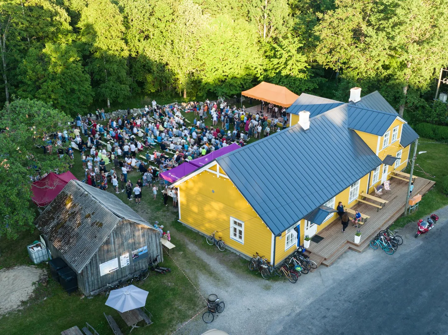 See kollane maja on Juminda poolsaare keskpunkt. Tavaelus asub seal Leesi pood ehk kogukonnapood, aga pidupäevadeks koguneb rahvas sinna kontserdile ja jaanipäevapeole. Fotojäädvustus on ansambli Kukerpillid suvekontserdilt 2022. aasta jaaniajal Leesi poe tagahoovis.