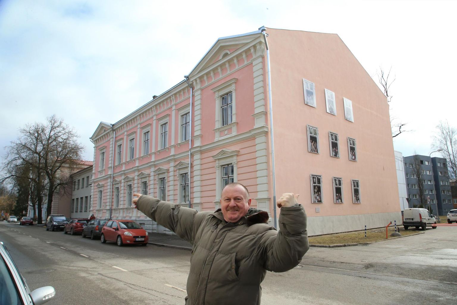 Alar Madisson osutab kirjandusmuuseumi ees parema käe näpuga aknale, millel ta kirjanikke pildistas, ja vasaku käega seinale, millele on kinnitatud pildistamise tulemus.