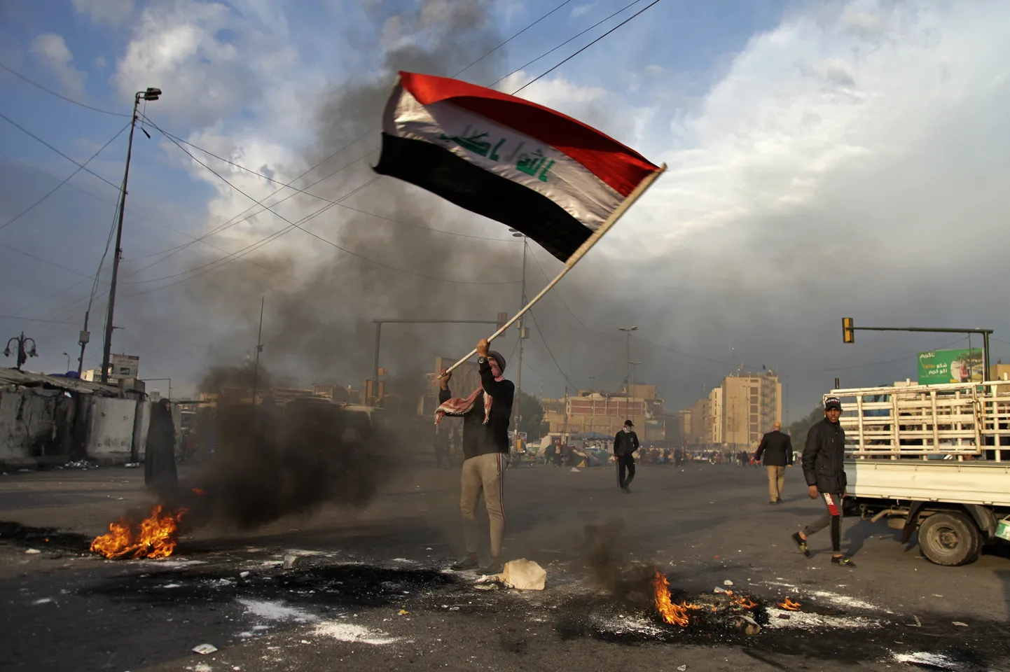 A protester waves the national flag while demonstrators set fire to close streets near Tahrir Square during a demonstration against the Iranian missile strike in Baghdad, Iraq, Wednesday, Jan. 8, 2020.