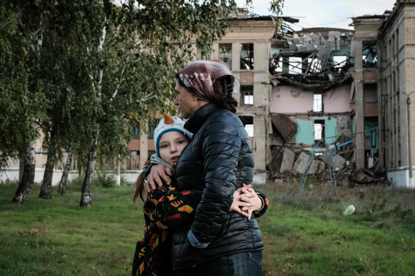 51-летняя Ольга Средненякова (справа), мать-одиночка восьмерых детей, обнимает младшую дочь Веру, 8 лет. На заднем плане разрушенная школа в Константиновке Донецкой области.