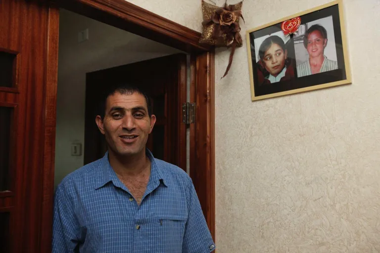 Басам Арамин стоит в дверном проеме, а на стене висят фотографии его дочери и дочери Рами