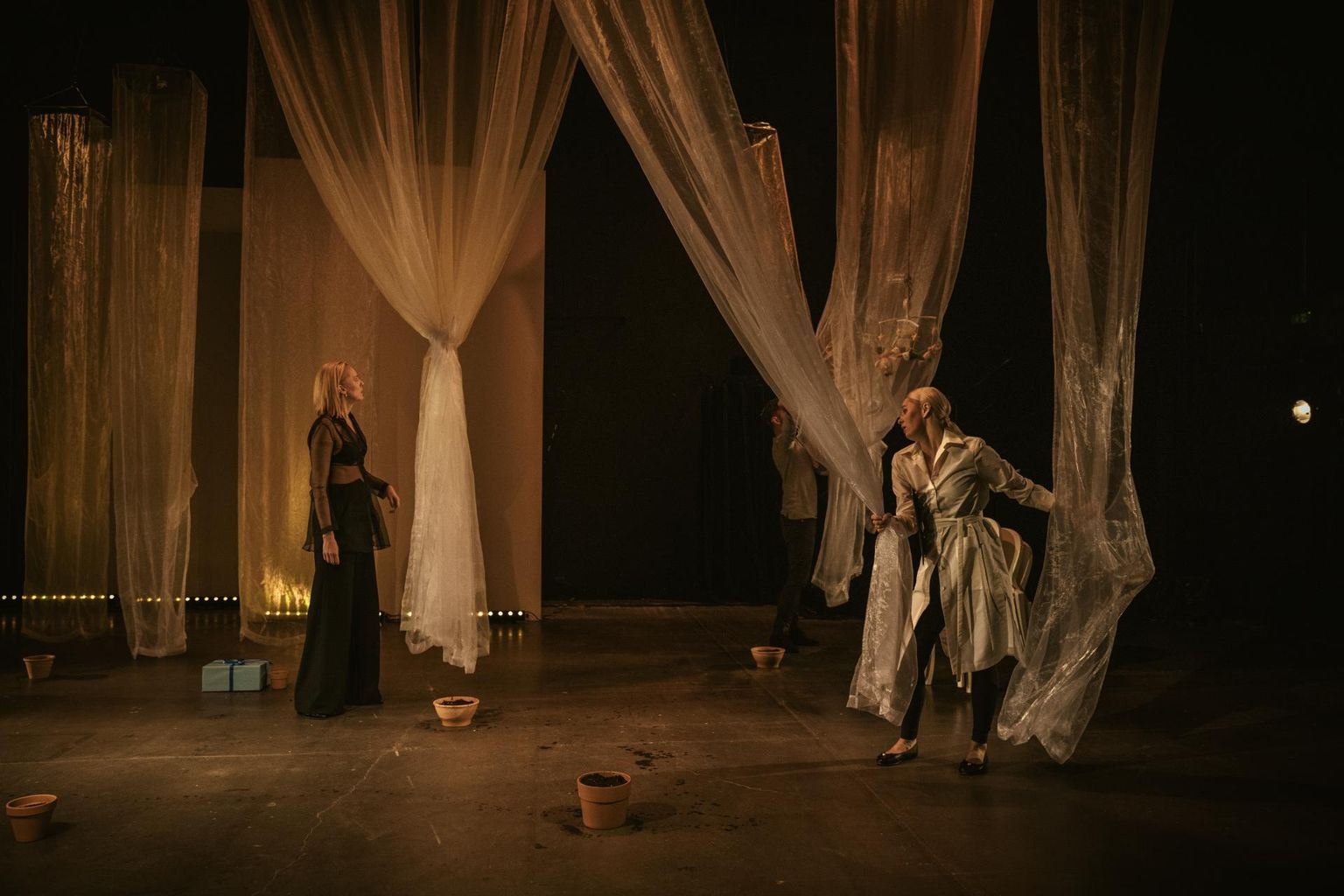 Näidendi «Võrsed» peategelane Paula (Ragne Pekarev, vasakul) ja ta pikaajaline elukaaslane (Kärt Tammjärv) räägivad oma lugu laval, kus on väheste rekvisiitide ja mööbliga abstraktne ruum, mille laest ripuvad sammastena läbipaistvad kardinad.