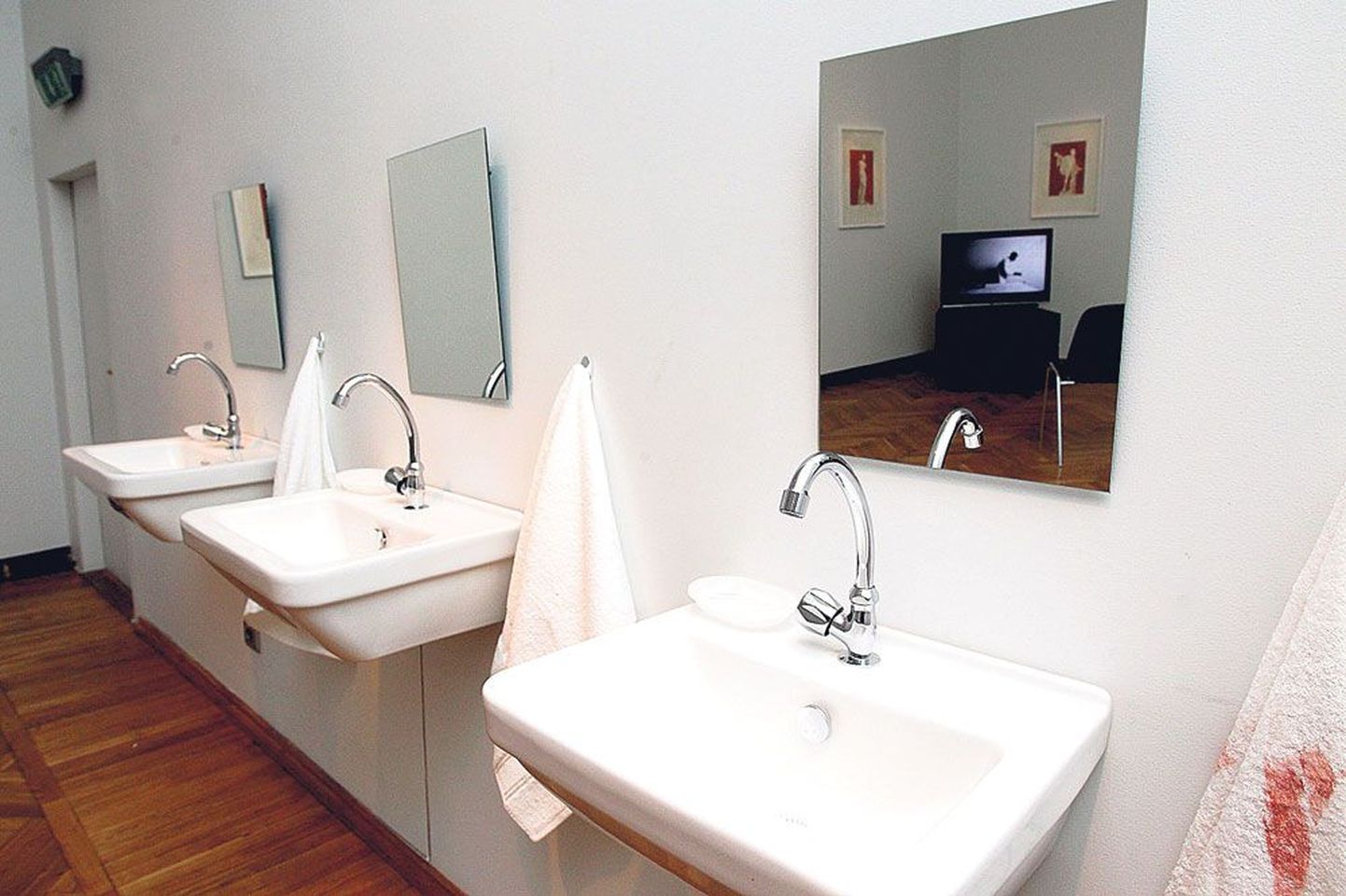 Raeplatsi viltuse maja kunstikabinetis on kraanikausi kohal peegel, millest paistavad samasse näituseruumi paigaldatud videoseadmed ja seinale kinnitatud joonistused.