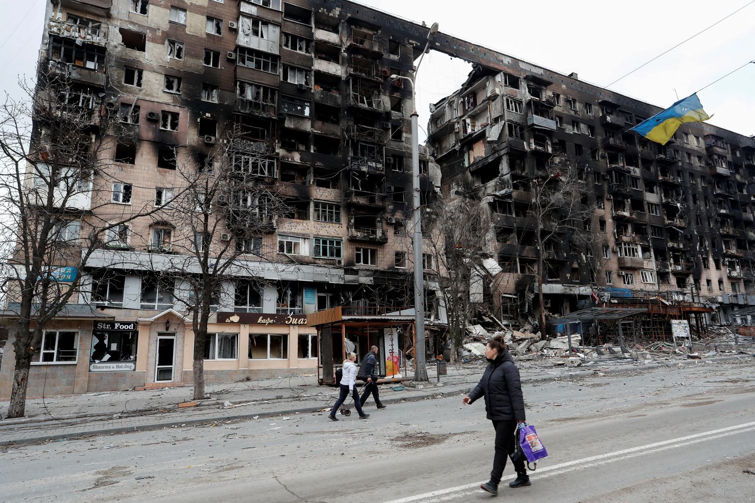 Inimesed kõndimas Ukrainas Mariupolis tänaval. Näha on sõjas kannatada saanud hooneid ja Ukraina lippu. Foto on tehtud 14. aprillil 2022