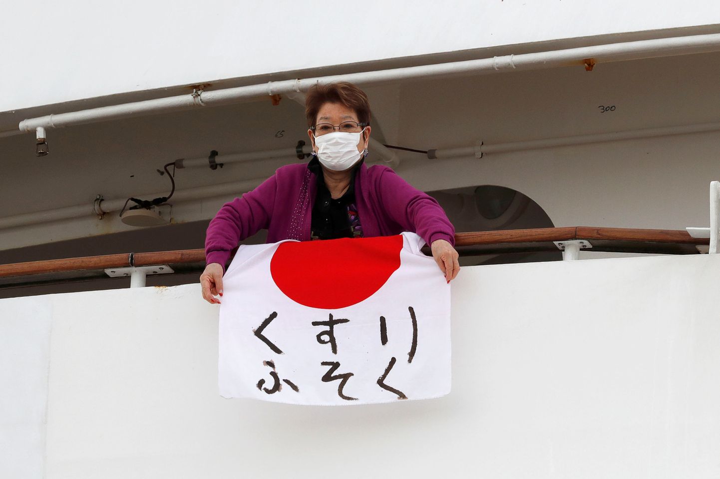 Kruiisilaeval Diamond Princess karantiinis olev naine hoiab Jaapani lippu, millele on kirjutatud, et «ravimeid napib»