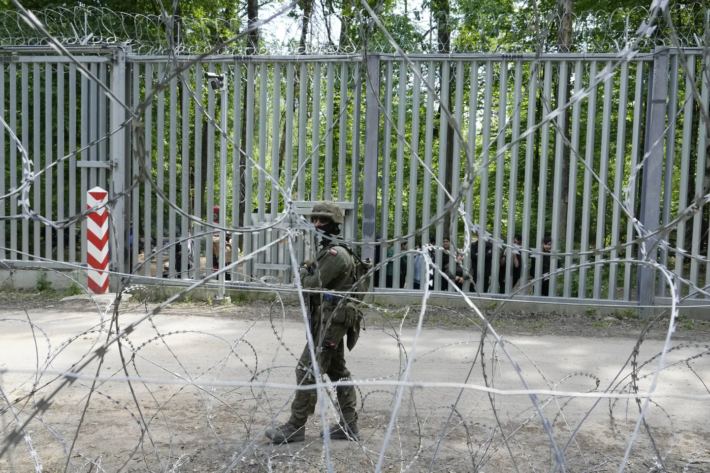 Польский солдат патрулирует забор на польско-белорусской границе, за которым видны мигранты.