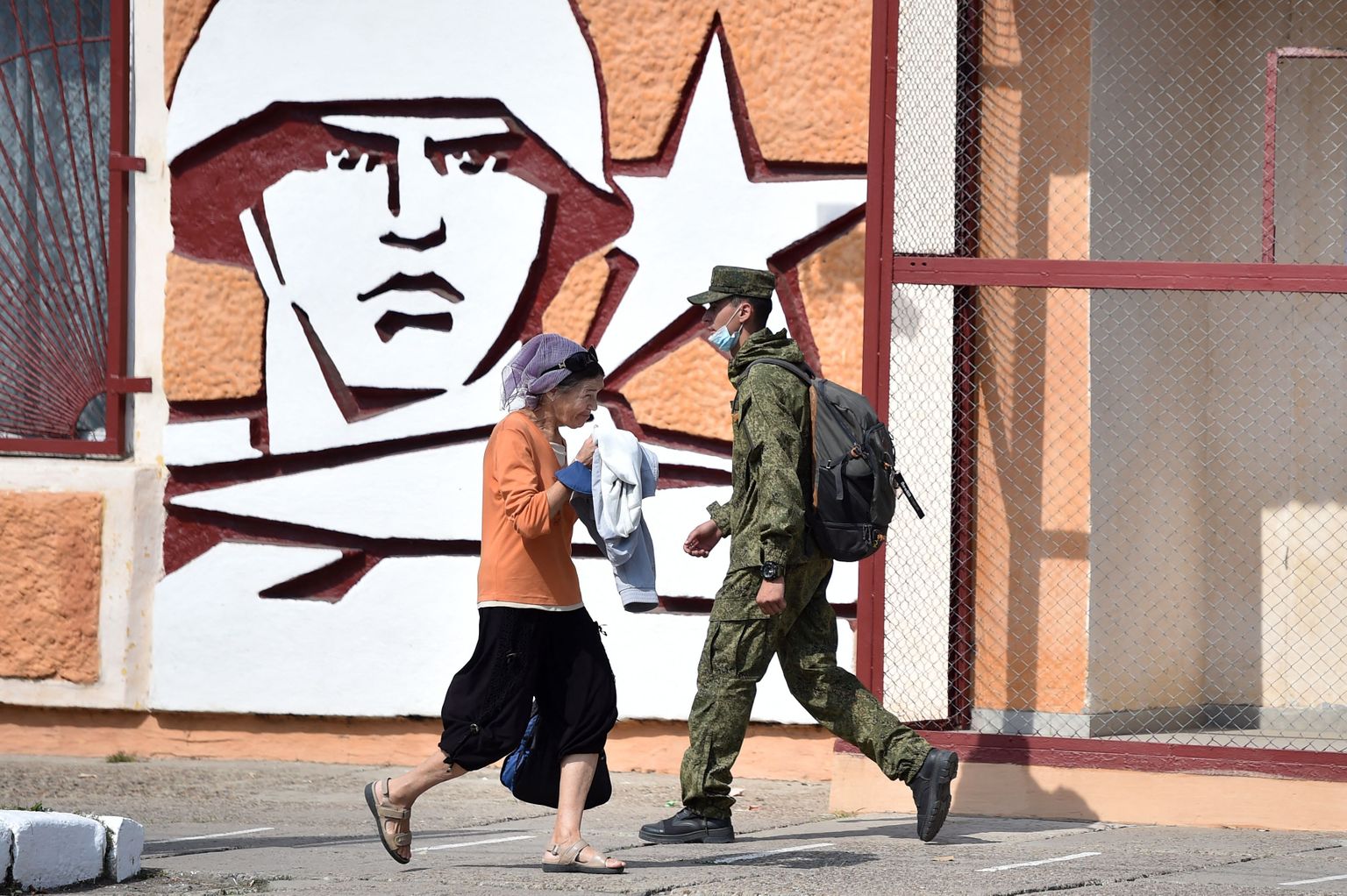 Солдат и женщина проходят мимо штаба оперативной группы ВС РФ в г. Тирасполе, столице самопровозглашенной Приднестровской Молдавской республики, 2021 год. (Photo by Sergei GAPON / AFP)